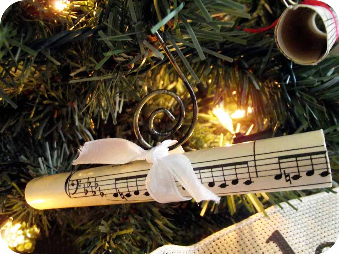 Muzyczne ozdoby bożonarodzeniowe: na zdjęciu kartka z nutami i biała wstążka na gałązce choinki